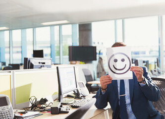 Portrait businessman holding smiley face printout over his face in office