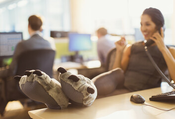 Businesswoman wearing wolf paw slippers feet up on desk talking on telephone
