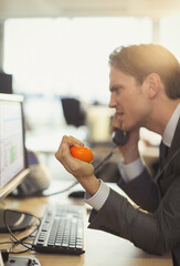Angry businessman squeezing stress ball talking on telephone at computer in office