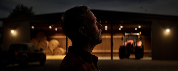 Silhouette portrait of 50s Caucasian male farmer standing near barn at dawn © ivanbaranov