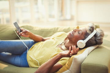 Comfortable mature woman listening to music headphones mp3 player on living room sofa