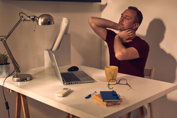 Man with head and neck pain while working on a laptop at home.