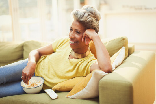 Comfortable mature woman watching TV eating popcorn on living room sofa