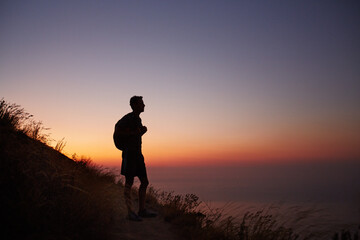Fototapeta na wymiar Silhouette of male hiker on trail overlooking ocean at sunset