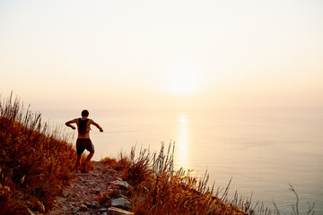 Male runner backpack descending craggy trail overlooking sunset ocean