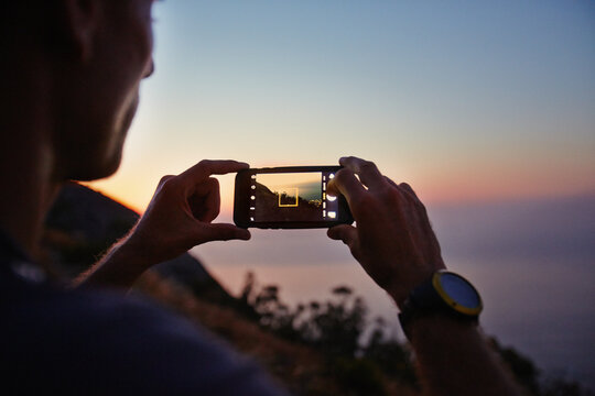 Man photographing sunset ocean view with camera phone