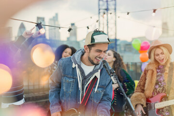 Enthusiastic musician playing guitar and singing at rooftop party