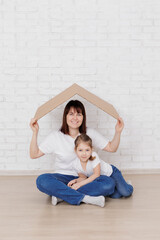 Happy woman and little girl sitting under cardboard roof at home