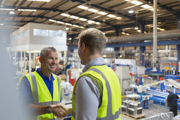 Smiling supervisor and worker handshaking in steel factory - obrazy, fototapety, plakaty