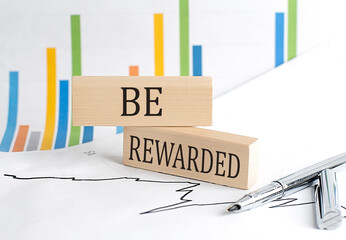 BE REWARDED text on a wooden block on chart background , business concept