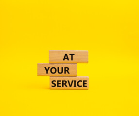 At your service symbol. Wooden blocks with words At your service. Beautiful yellow background. Business and At your service concept. Copy space.