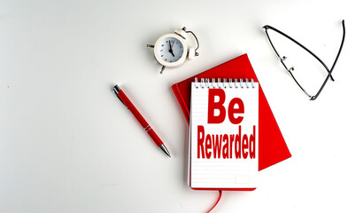 BE REWARDED text on notebook , red pen and notebook, business concept, white background