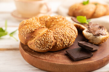 Homemade sweet bun with chocolate cream and cup of coffee on a white wooden. side view, selective focus.