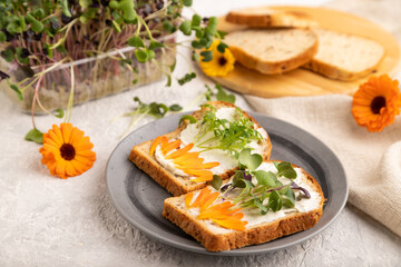 White bread sandwiches with cream cheese, calendula and microgreen on gray. side view, selective focus.
