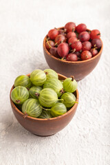 Fresh red and green gooseberry in clay bowl on gray concrete, side view.