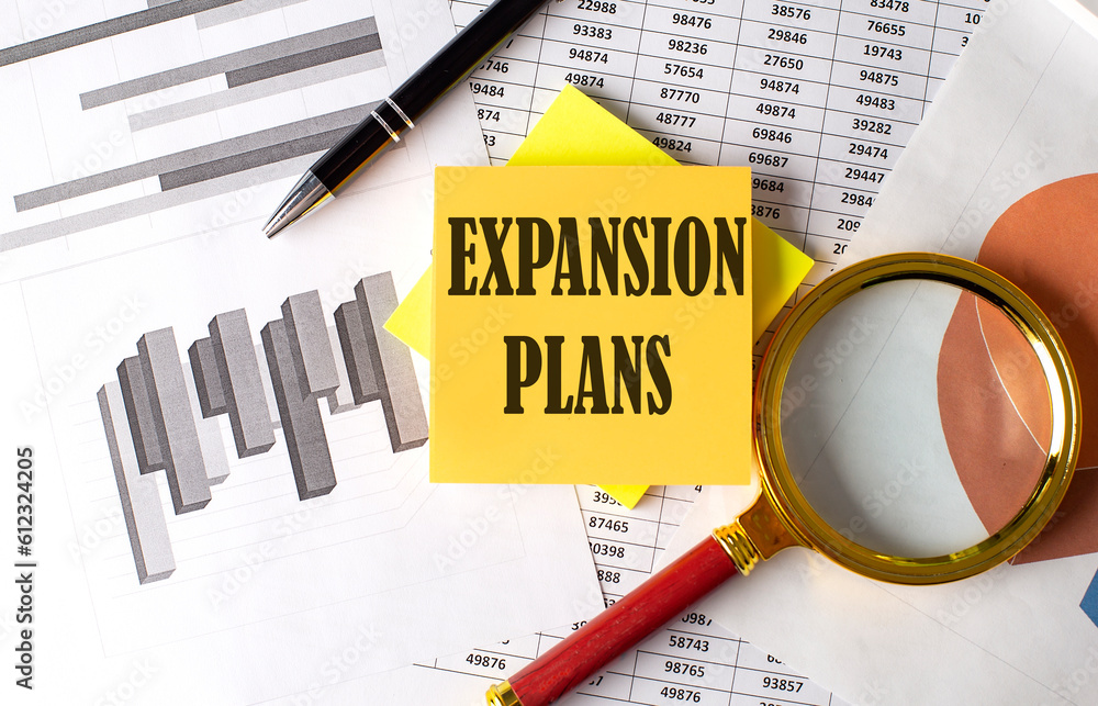 Aufkleber expansion plans text on a sticky on the graph background with pen and magnifier