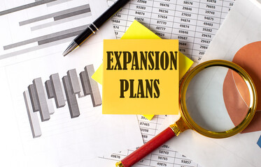 EXPANSION PLANS text on a sticky on the graph background with pen and magnifier