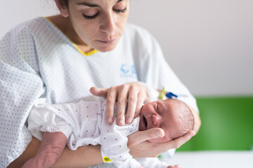 young mother who has just given birth in the maternity hospital holds her newborn baby upside down in her arms to avoid gas and colic. newborn baby health and care concept