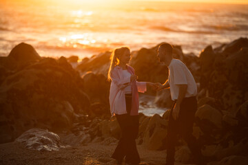 Fototapeta premium A young couple are playing on the beach during a golden sunset.