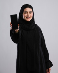 saudi arabian woman in hijaab standing with phone in hand and showing the screen with smile