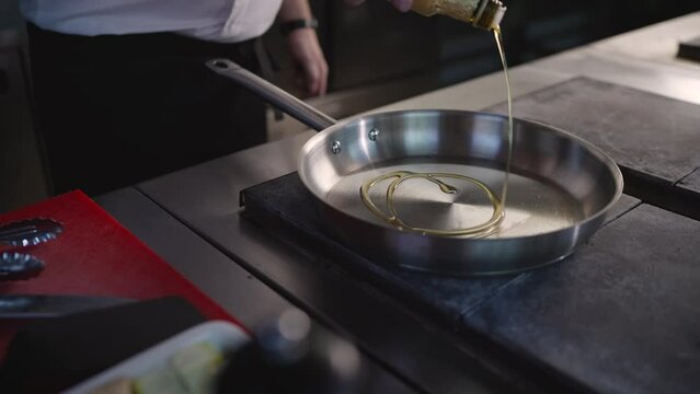 The chef pours oil into a hot pan in a professional kitchen cooking in a restaurant. Close-up of a cook pouring oil into a frying pan.