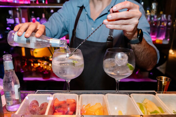 Professional barman is making cocktail at night club or bar. Preparation of gintonic cocktail on the bar counter against the background of bartenders.