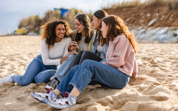 Young multiracial women laughing out loud on a sunny day - Cheerful group female friends enjoying summer vacation together on the beach sitting down- Summer vacation