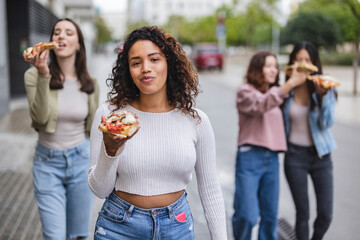 beautiful female friends eating pizza on the street, in the tourist city, focus on curvy latina woman. - obrazy, fototapety, plakaty