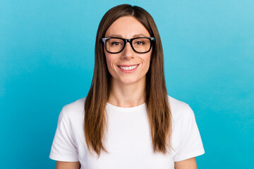 Close up happy young woman wearing eyeglasses showing toothy smile at camera against blue wall background