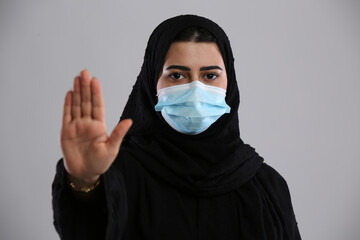 saudi arabian woman in hijaab wearing mask looking at camera with stop sign