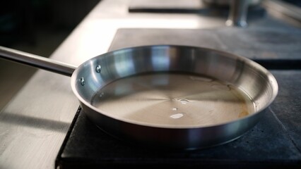 The chef pours oil into a hot pan in a professional kitchen cooking in a restaurant. Close-up of a cook pouring oil into a frying pan.
