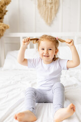 a little cute girl child on a white cotton bed at home is fooling around playing with tails and...