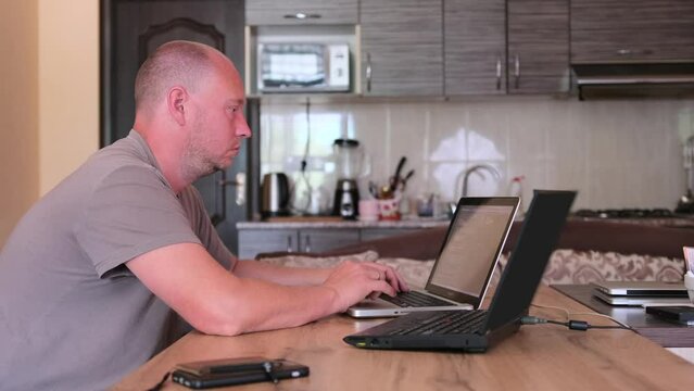 Side view man working on two laptops typing program code on keyboard. IT specialist, programmer work in home office. Freelancer and work at home concept.
