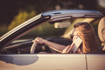 A woman talking on the phone while driving in a convertible.