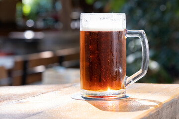 A glass of cold light beer with foam is on the table in the summer cafe. Close up, copy space.