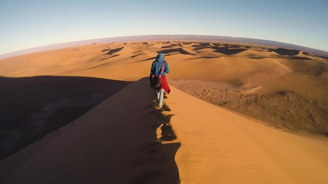 A person walks over a giant dune of sand