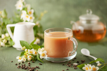 Composition with cup of jasmine milk tea and flowers on green background