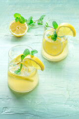 Lemonade with mint. Lemon water drink with ice. Two glasses on a blue background. Detox beverage. Fresh homemade cocktail