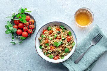 Quinoa tabbouleh salad in a bowl, a healthy dinner with tomatoes and mint, with a drink, overhead flat lay shot