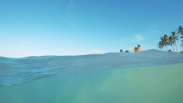 Half underwater slow motion clear blue sea water at the tropical beach at sunset. Idyllic view of ocean and white sand coast with palm trees 