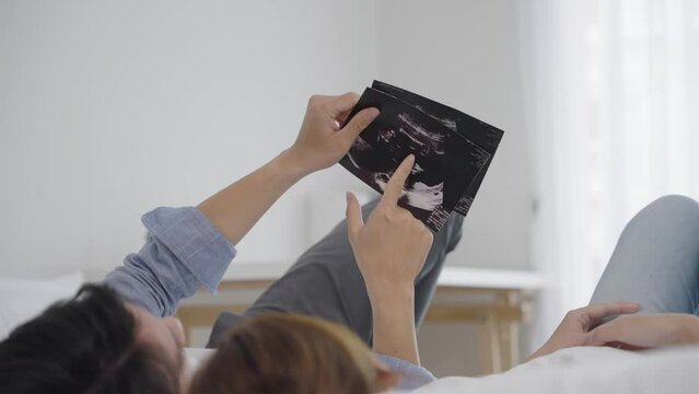 an Asian parent eagerly examining ultrasound photos of their unborn baby, a bond between parent and child, a testament to the miraculous journey of new life, happy couple looking at ultrasound photos
