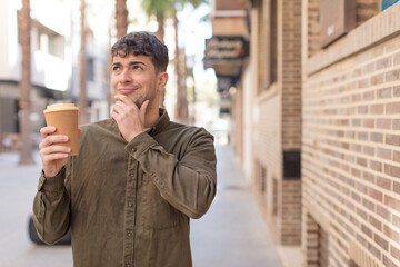 young handsome man smiling with a happy, confident expression with hand on chin. take away coffee concept