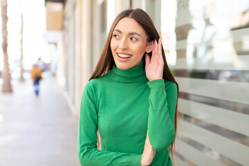 young pretty woman looking happy, listening, trying to hear a secret conversation or gossip,...