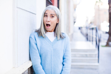 senior retired pretty white hair woman looking very shocked or surprised, staring with open mouth...