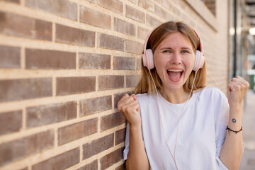 young pretty woman feeling shocked,laughing and celebrating success. headphones and music concept