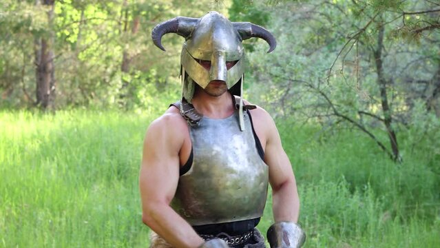 Portrait of a warrior in a horned helmet, a steel breastplate with a two-handed ax in his hands, posing against the backdrop of the forest. Smooth camera movement.