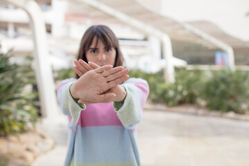 pretty young woman covering face with hand and putting other hand up front to stop camera, refusing...