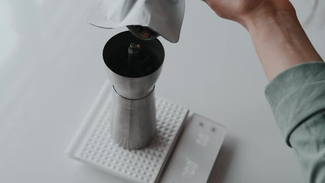 Close up video of woman putting coffee beans in manual grinder.