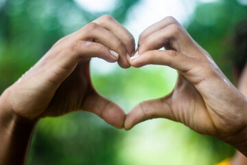 A young man shows his both hand with signs of love and a background blur