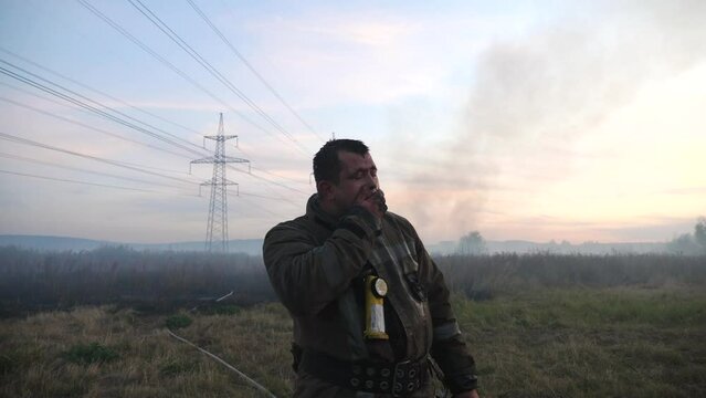 Male tired firefighter wiping away the water on his face after hard work. Portrait of young fireguard in uniform after fire at countryside. Concept of saving lives and heroic profession. Slow mo